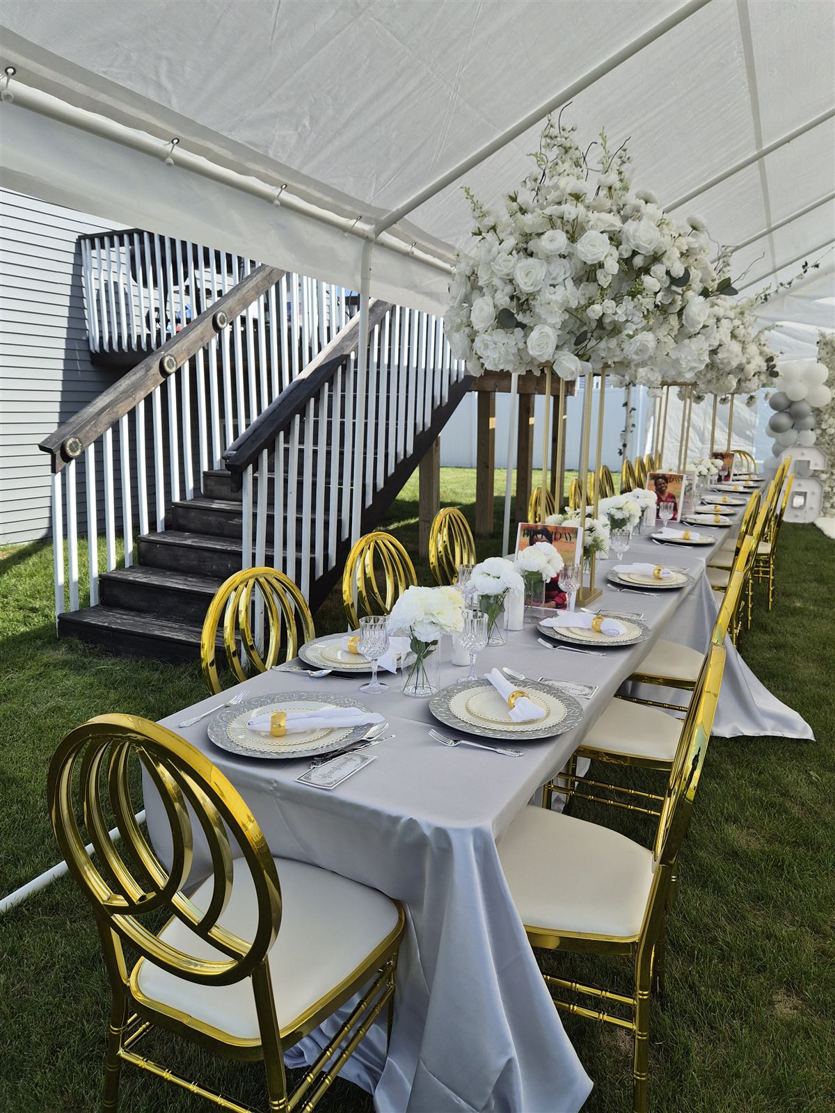 Long tented reception table with gold ring-back chairs and tall white floral centerpieces on gold stands